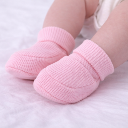 Baby wearing organic cotton pink baby booties on a soft surface