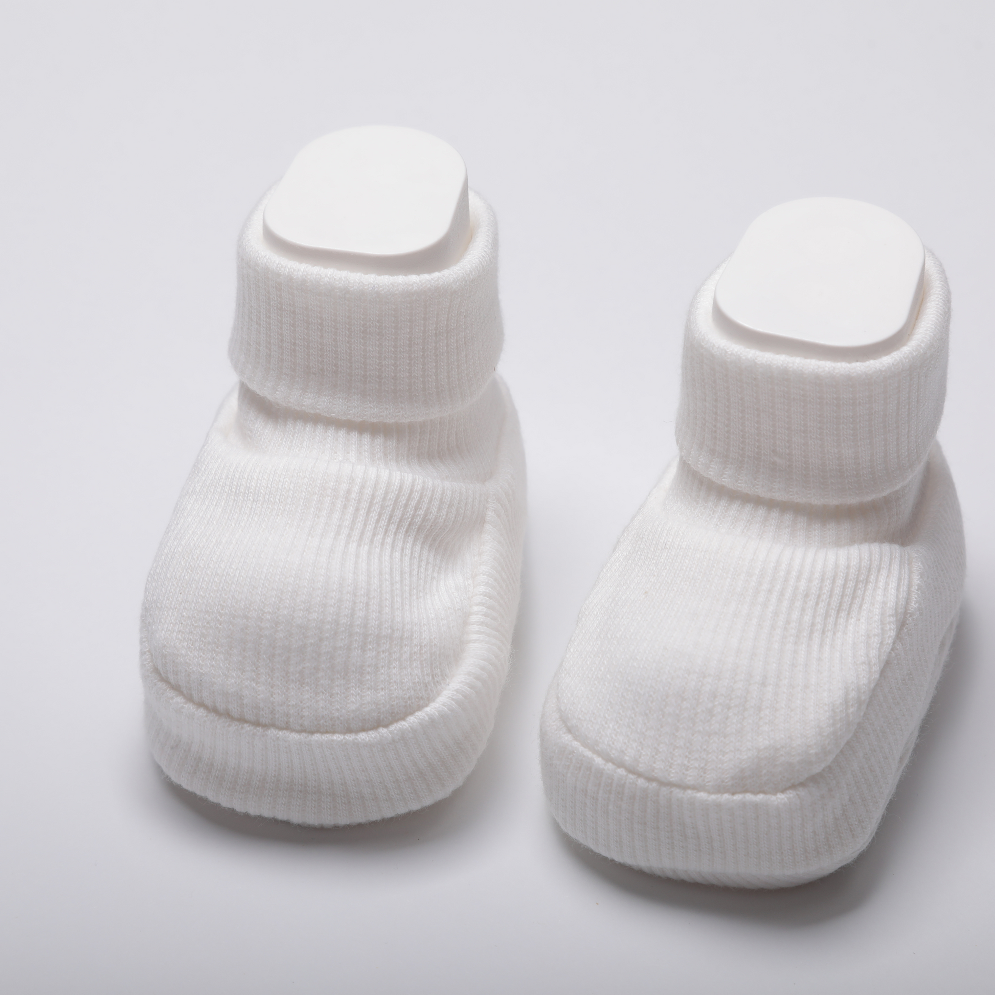 Newborn baby wearing organic cotton white baby booties while sleeping on a soft white blanket