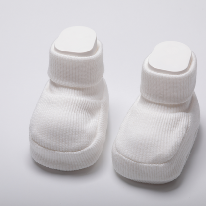 Newborn baby wearing organic cotton white baby booties while sleeping on a soft white blanket