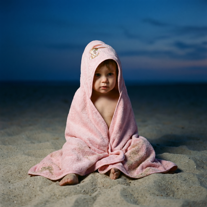 Child wearing a pink organic cotton hooded baby bath towel at the beach
