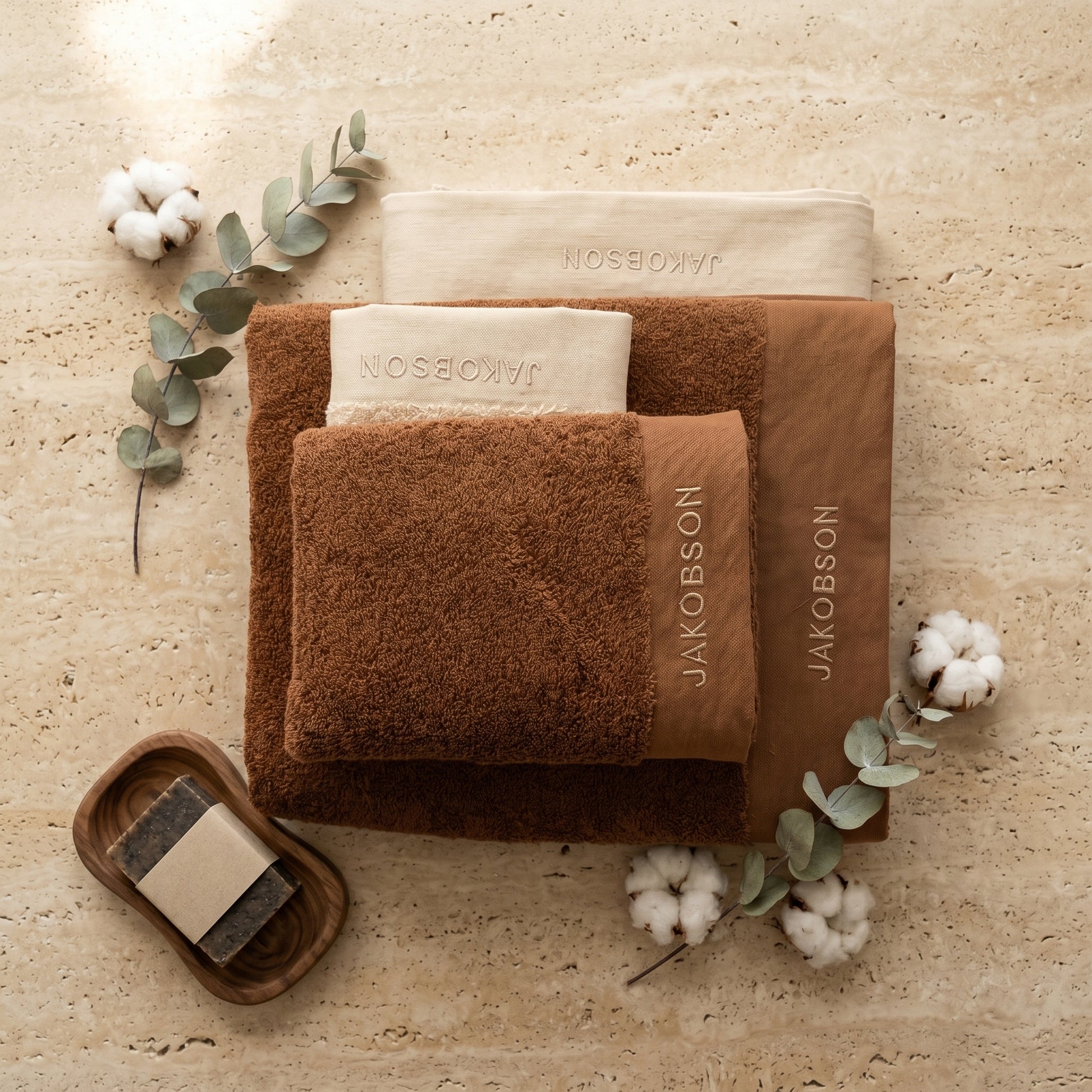 4-piece organic cotton towel set in cinnamon with Jakobson branding displayed with cotton and eucalyptus leaves