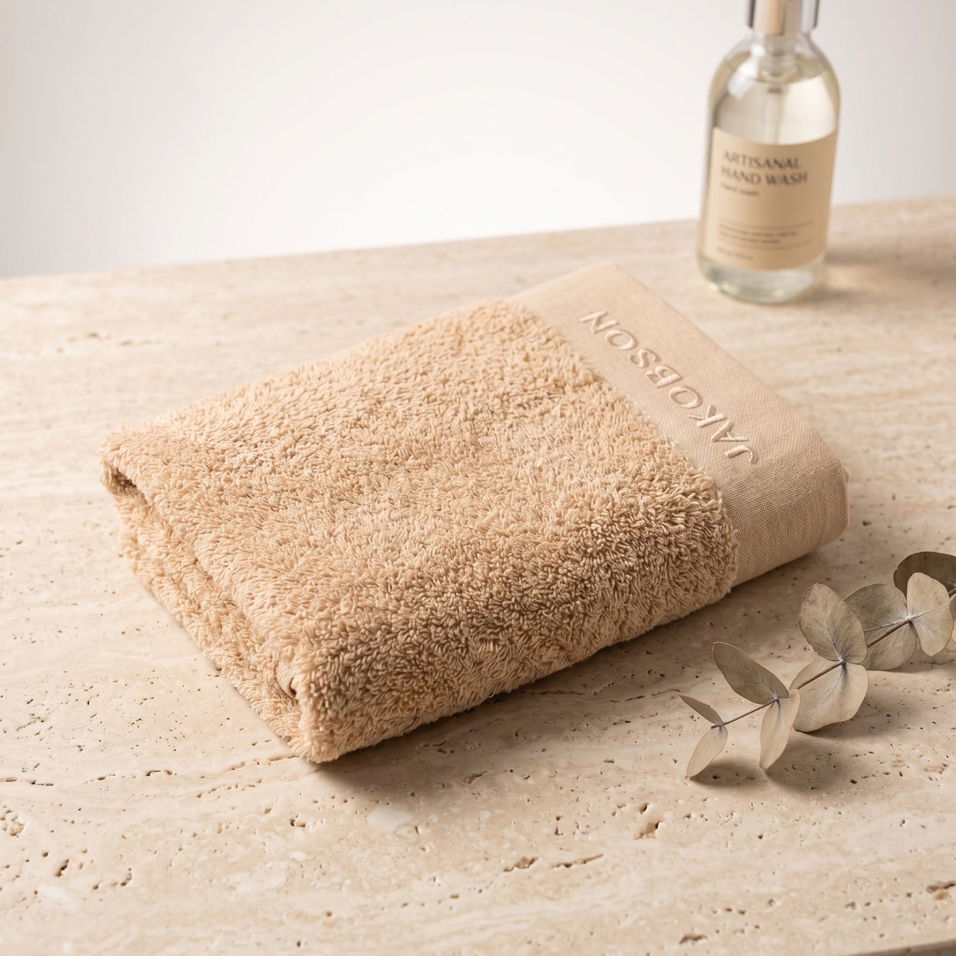 Organic cotton terry bath towel in beige with Jakobson branding displayed on a wooden surface