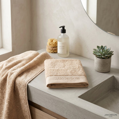 Organic cotton terry bath towel in beige displayed with soap, sponge, and bathroom accessories