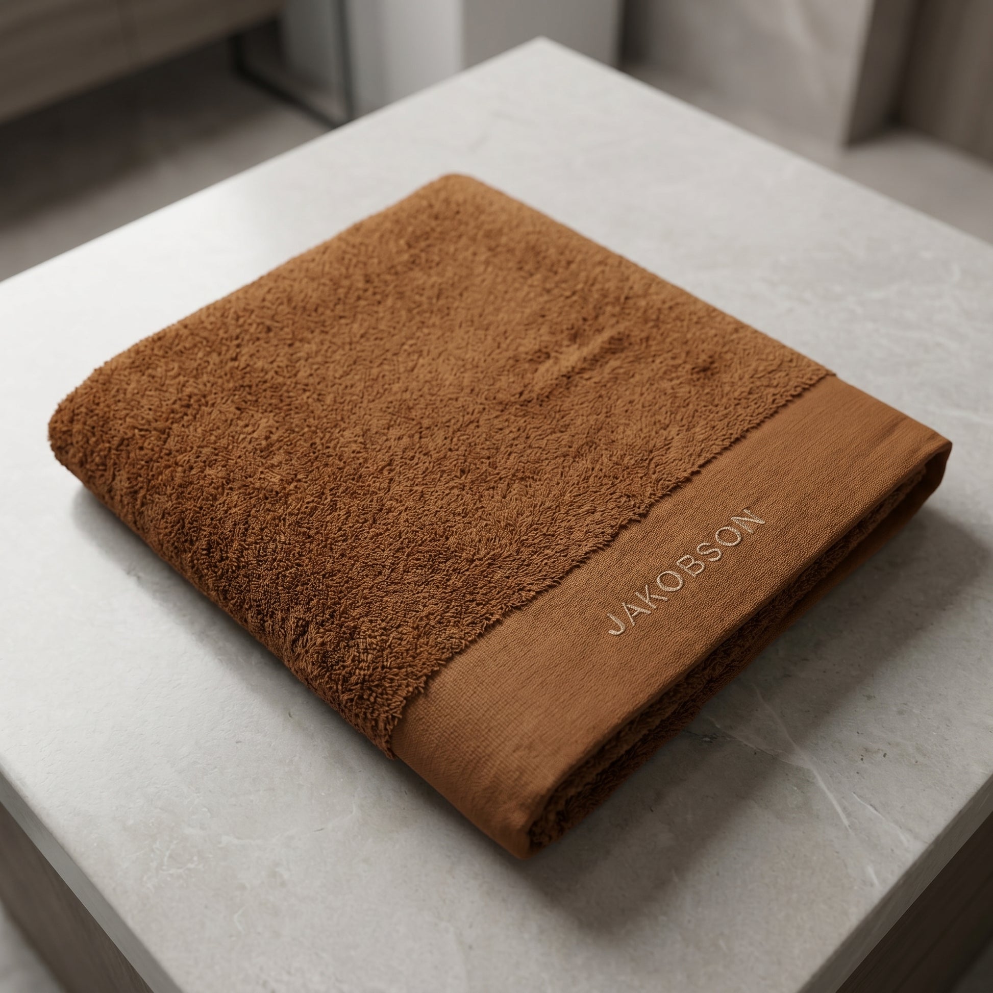 Organic cotton terry bath towel in cinnamon with Jakobson branding displayed on a marble surface