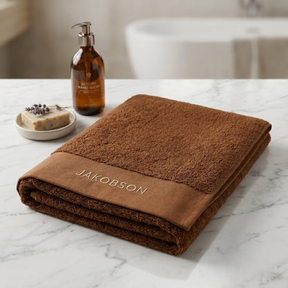 Organic cotton terry bath towel in cinnamon with Jakobson branding displayed with soap and bath accessories
