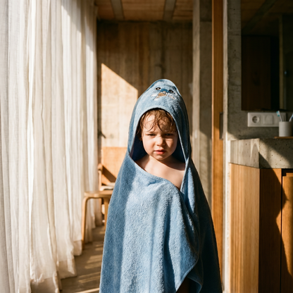 Child wearing a blue organic cotton hooded baby bath towel in a bathroom