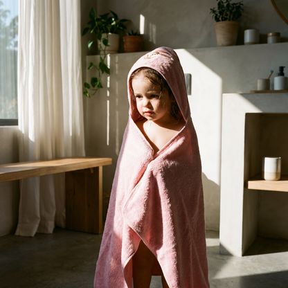 Child wearing a pink organic cotton hooded baby bath towel indoors